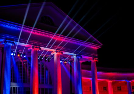Illuminierte Wandelhalle mit ionischen Säulen in rotem und blauem Licht bei den Parklichter 2024 unter dem Motto „Very British“, mit sichtbaren Scheinwerfern.