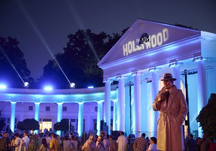 Hollywood-Projektion auf der blau illuminierten Wandelhalle mit Detektiv-Figur und Publikum bei den Parklichtern 2022 unter dem Motto „Unforgettable – die größten Film- und Musicalhits“.