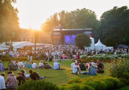 Abendatmosphäre bei den Parklichtern am Samstag zum Veranstaltungsmotto "Feel the 90s". Zahlreiche Besucher liegen bei strahlender Abendsonne auf den grünen Wiesen im Kurpark und lauschen dem Konzert der Söhne Mannheims auf der Hauptbühne zu.