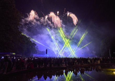 Musik-synchrones Höhenfeuerwerk mit gelben und blauen Lichteffekten bei den Parklichtern 2025 in Bad Oeynhausen, Publikum blickt in den Himmel, Spiegelung im Brunnen.