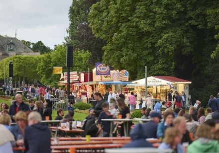 Verkaufsstände und Publikum auf Sitzgarnituren im Kurpark bei den Parklichtern 2023 in Bad Oeynhausen