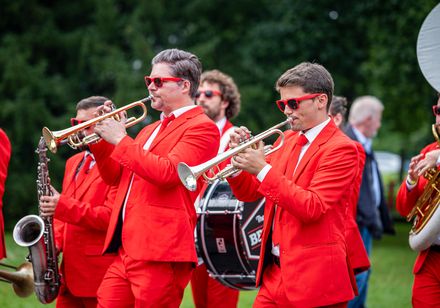 Brass Band in auffälligen roten Anzügen spielt Trompeten und Saxofon bei den Parklichter 2024 unter dem Motto „Very British“ im Park.