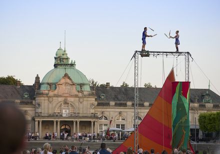 Artisten jonglieren auf einer hohen Bühne vor dem historischen Kurhaus bei den Parklichtern 2022 unter dem Motto „Unforgettable – die größten Film- und Musicalhits“.