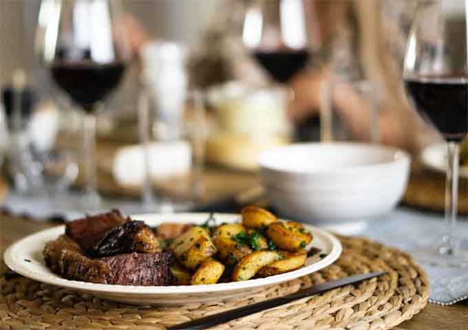 Gedeckter Tisch mit Bratkartoffeln, Fleisch und gefüllten Rotweingläsern 